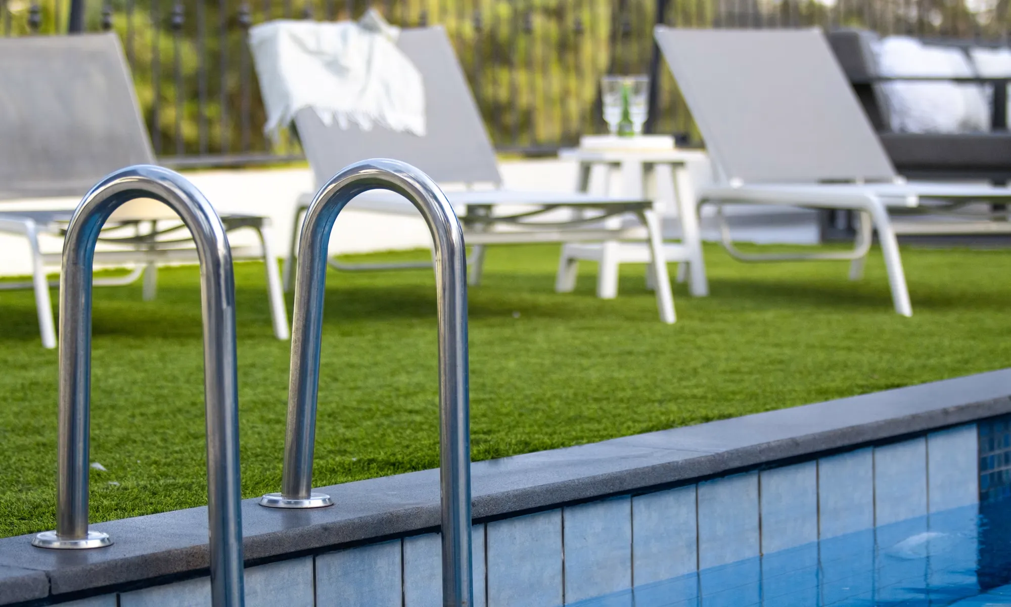 Realistischer Kunstrasen verlegen auf einer modernen Terrasse mit Swimmingpool und Liegestühlen